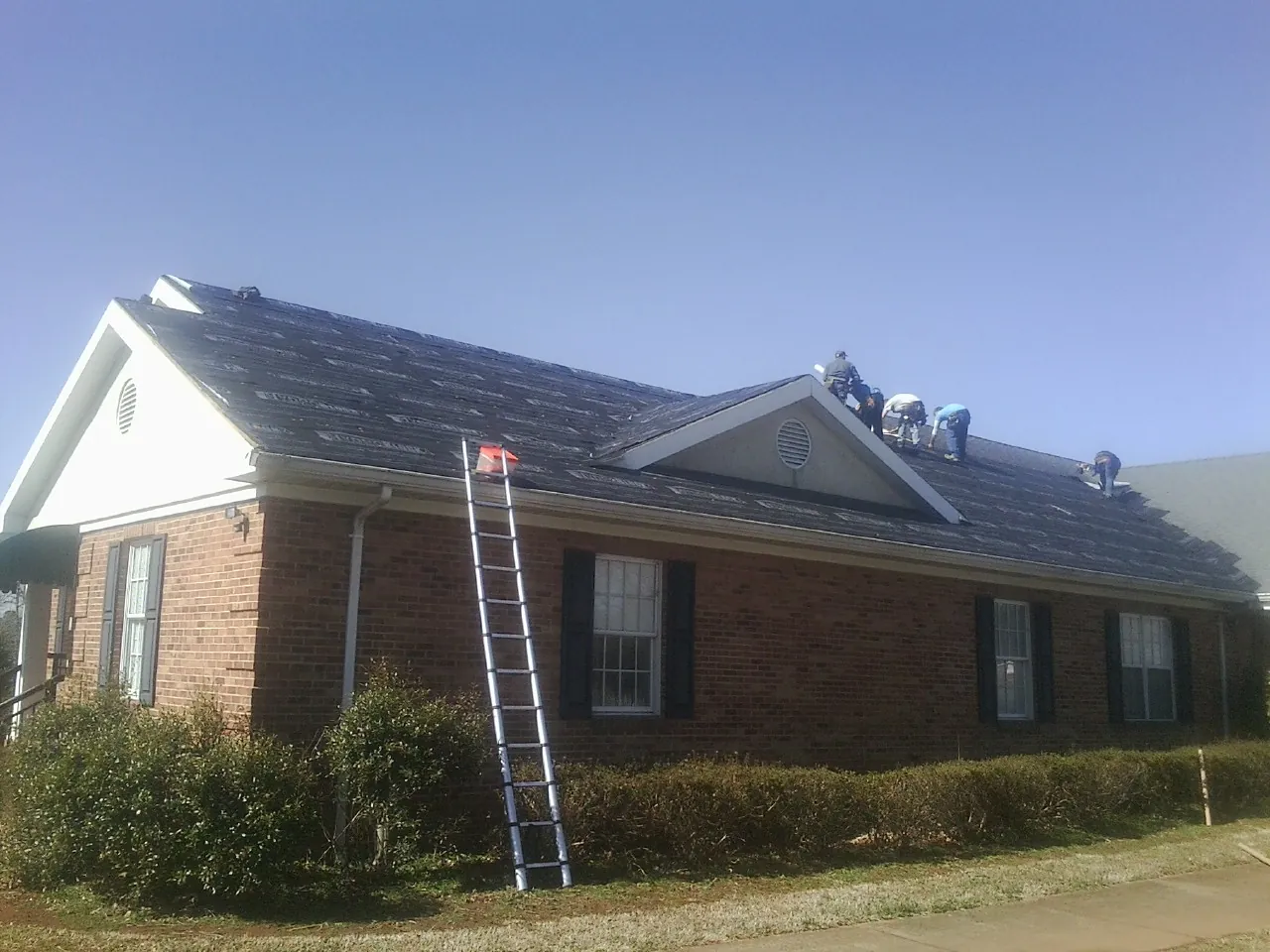 Crew tearing shingles off a brick ranch roof with a ladder set — Metal Roof Repair work by our crew in Silverton