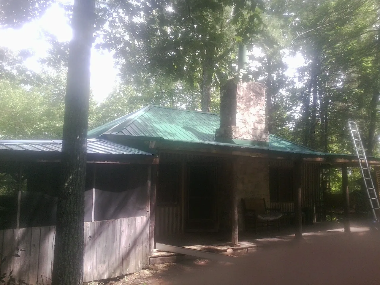Green metal roof and stone chimney above a log cabin porch in Silverton